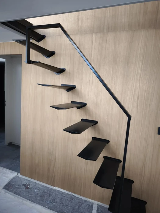 Escalier suspendu moderne dans un intérieur contemporain avec marches flottantes en métal noir fixées sur mur en bois clair