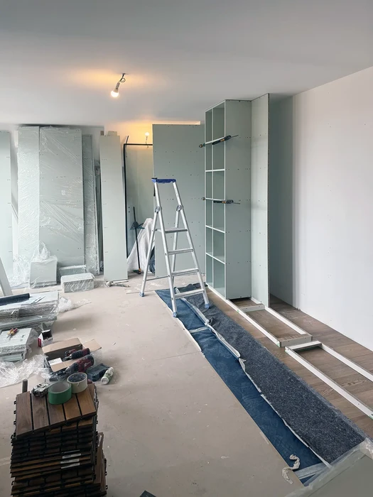 Chantier de rénovation intérieure en cours avec escabeau aluminium, parquet bois massif en pose, murs peints en vert sauge et blanc