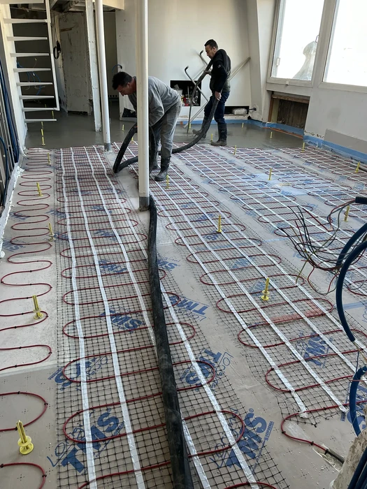 Deux ouvriers installent un système de chauffage au sol dans un appartement en rénovation