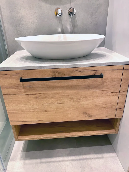 Salle de bain moderne avec meuble vasque suspendu en bois naturel, plan de travail en pierre claire, vasque ovale blanche posée, robinetterie murale chromée