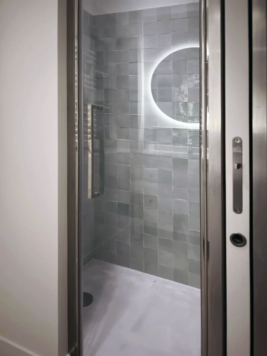 Salle de bain moderne sous combles avec baignoire îlot blanche, radiateur horizontal blanc, fenêtre à croisillons donnant sur jardin arboré